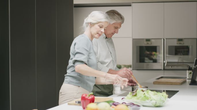 一对老年夫妇在家里的厨房里做饭。一个成熟的男人和女人一起做一顿健康的饭，享受一个放松的退休生活