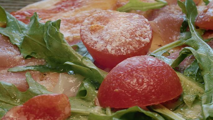 火腿披萨配斯特拉查特拉奶酪、西红柿和芝麻叶。在木桌上旋转