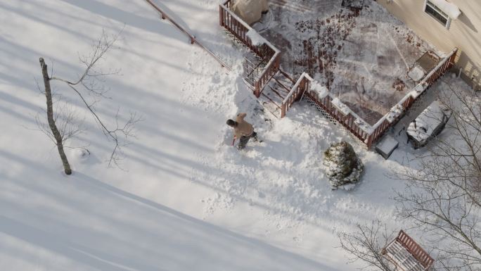 一名成年男子在冬季降雪后用铲子清理门廊的积雪。鸟瞰无人机视频正上方。
