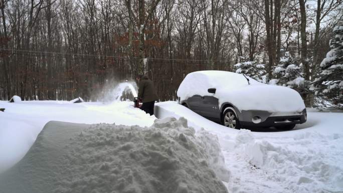 一名男子在冬季暴风雪后清理被雪覆盖的汽车周围的车道。
