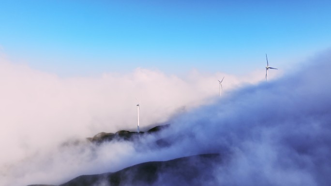 蓝色天空下云雾中高山上的风力发电机组