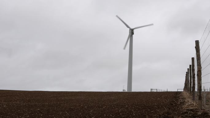 风力涡轮机在阴暗灰暗的耕地中转动