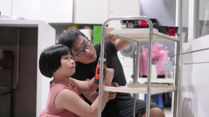 亚洲中国小女孩帮助父亲用无绳钻组装手推车托盘。DIY工作。
