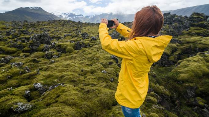 穿着黄色雨衣的游客在冰岛火山景观上拍摄苔藓覆盖物