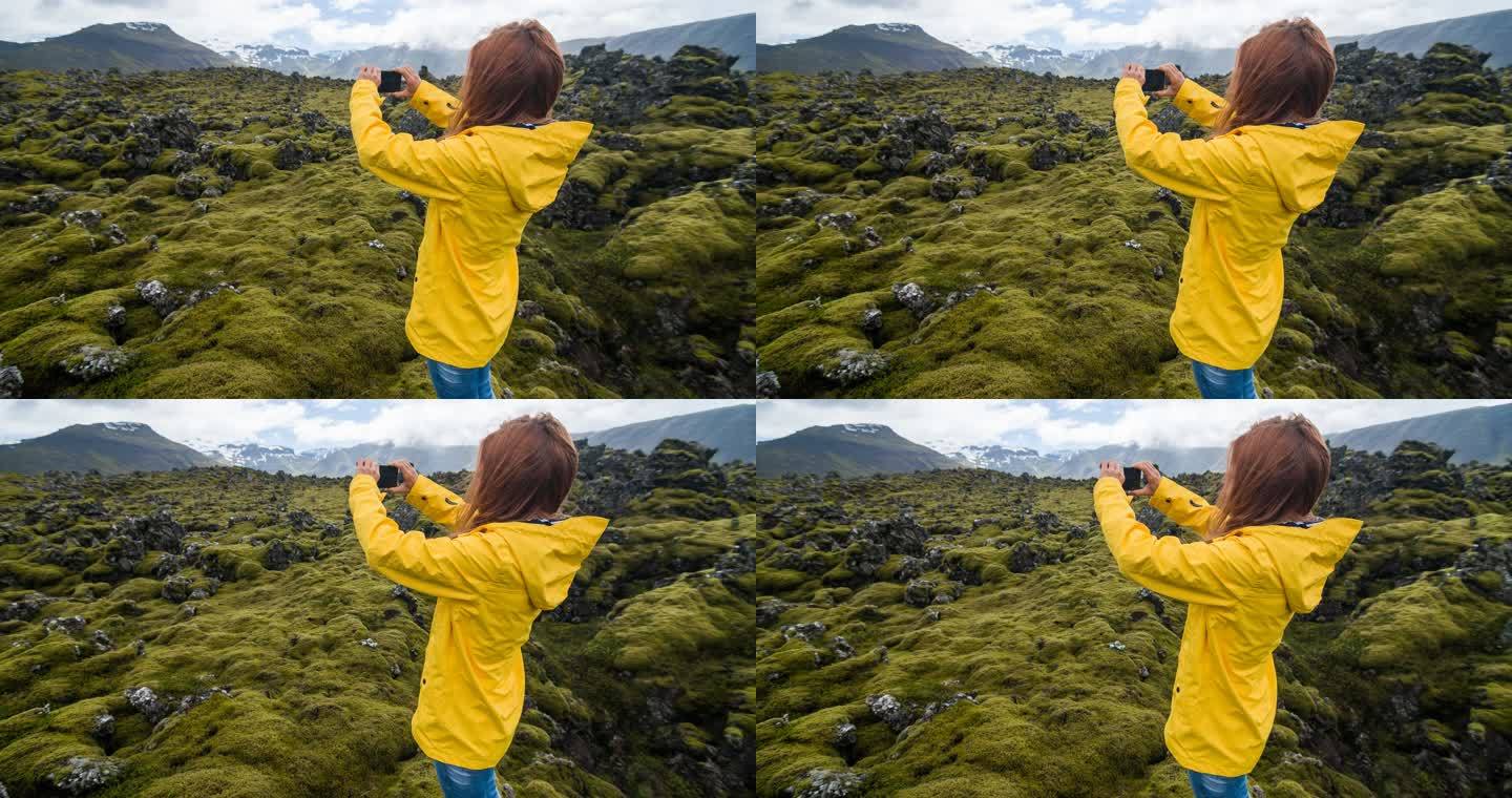 穿着黄色雨衣的游客在冰岛火山景观上拍摄苔藓覆盖物