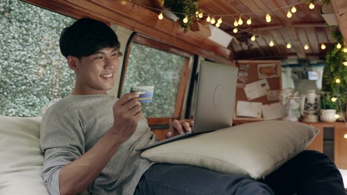 亚洲男性在露营车中使用电脑在线购物的场景，在线购物的概念