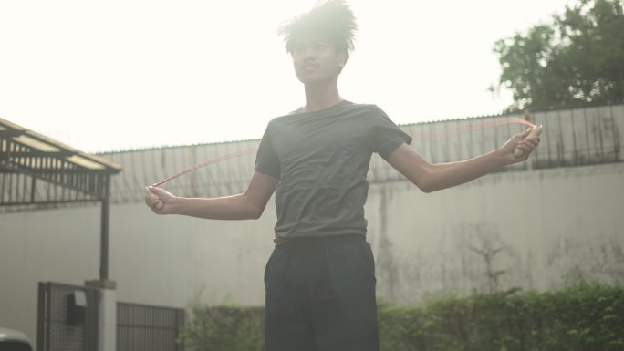 一名亚洲年轻男子凌晨在前院跳绳的慢镜头
