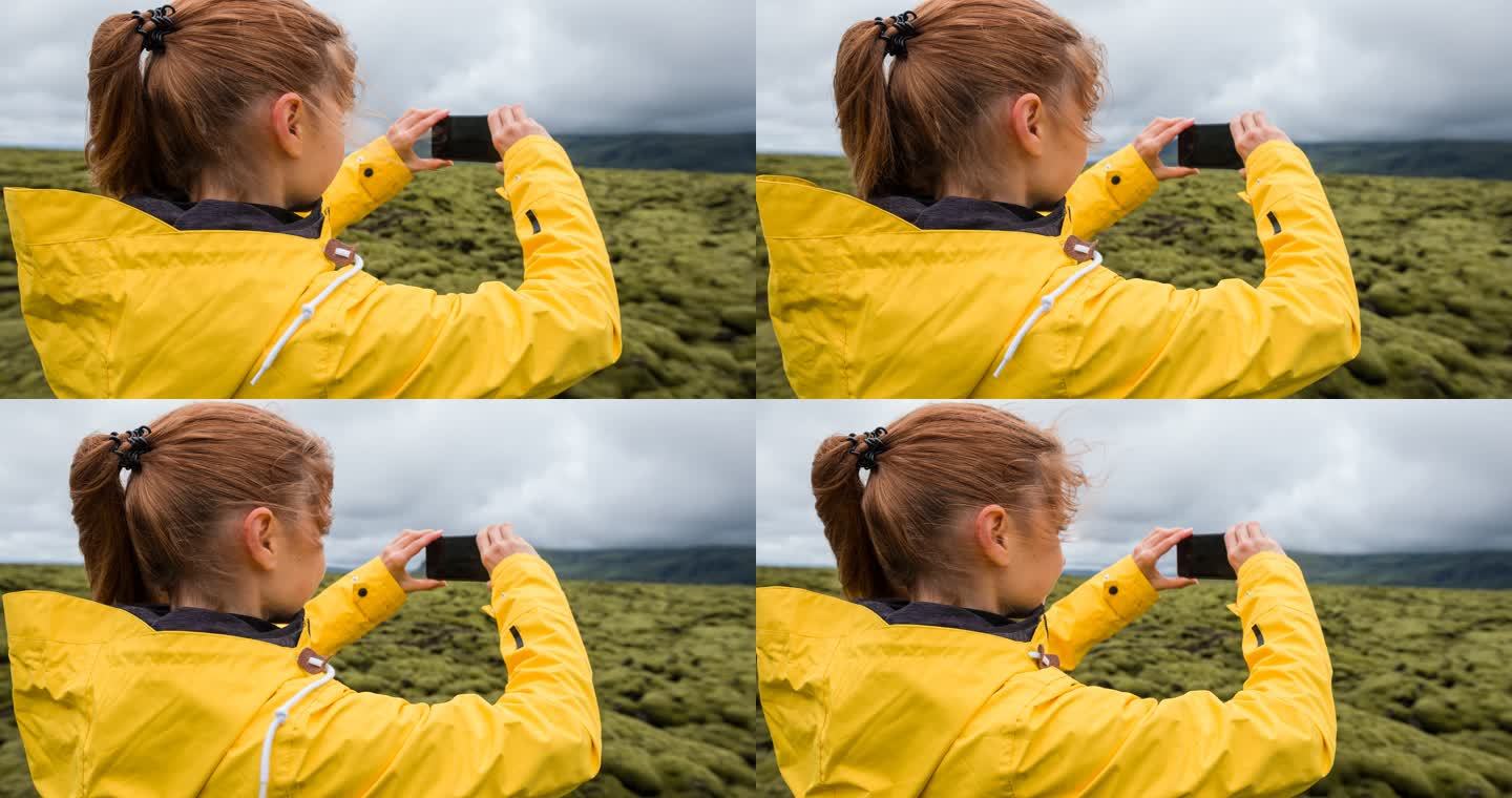 一位女性游客在大风天用智能手机拍摄绿色和苔藓的火山景观
