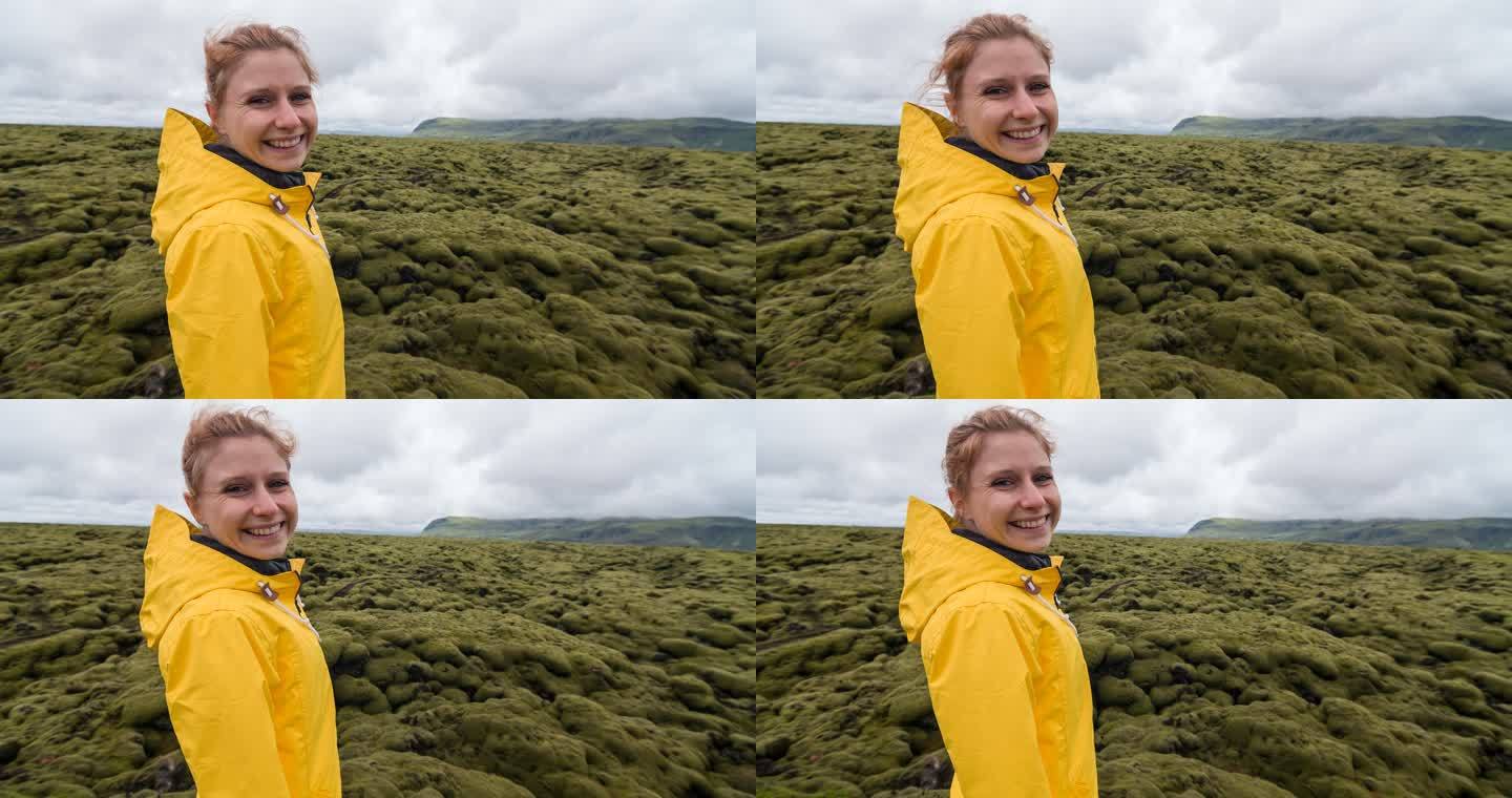 年轻的女游客在冰岛旅游，欣赏苔藓般的风景，对着镜头微笑