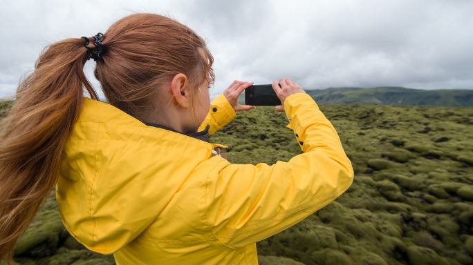 身穿黄色雨衣的女子在苔藓覆盖的熔岩场拍照