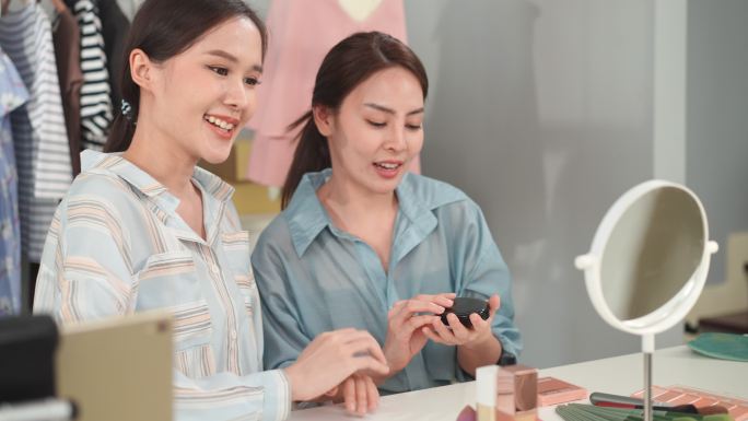 两个年轻漂亮的亚洲女孩正在为在线销售化妆品进行视频录制。亚洲女性化妆师在服装和化妆品店向网上顾客推荐