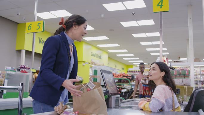 女收银员在超市收银台帮顾客打包食品杂货