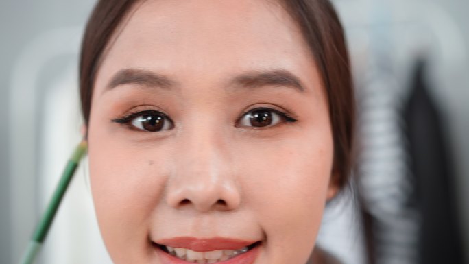 关注美丽的亚洲美容博主正在录制化妆教程和美容技巧，使用深棕色眼影放置在眼睛的折缝中，从而形成眼睛的尺