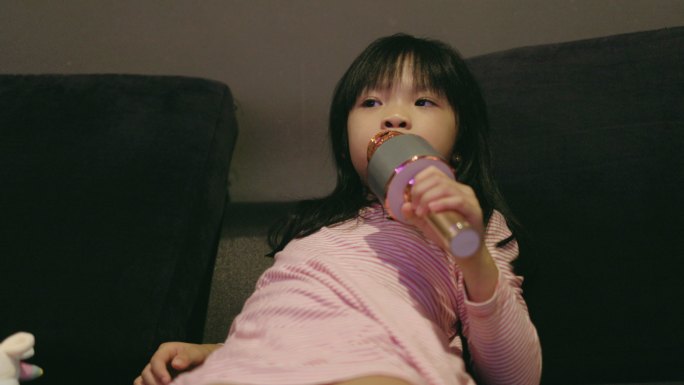 小可爱的女孩在她父亲的旁边唱歌，听客厅里的股票视频