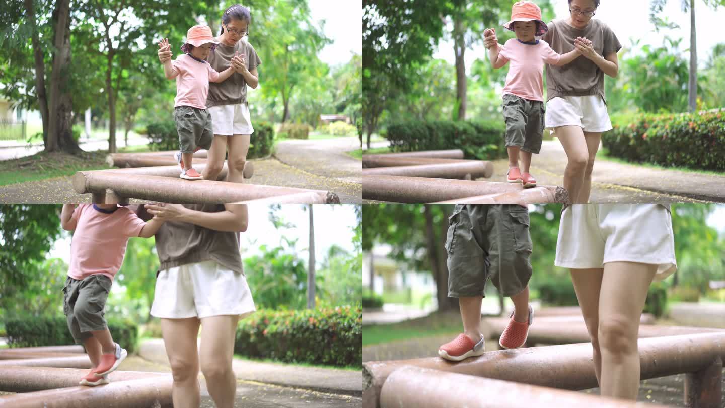 一个可爱的蹒跚学步的男孩在她妈妈的帮助下在公共公园的平衡木上行走
