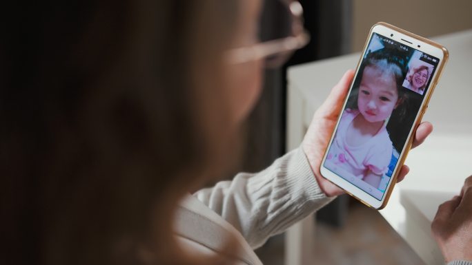 年长的成年人在家中通过智能手机与孙女进行视频通话。与远方的爱人保持联系，保持身体距离