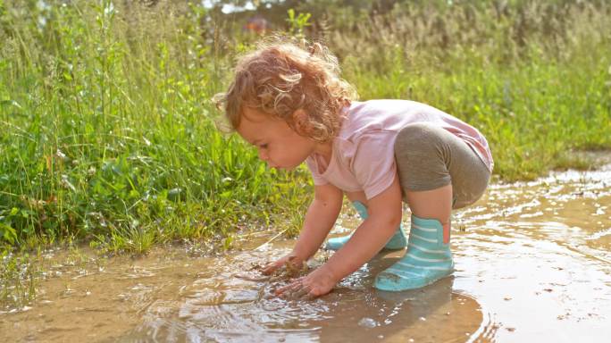 SLO MO小女孩在泥泞的水坑里玩她的手