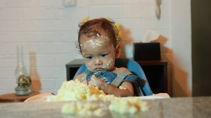 一名男婴在第一次生日派对上，脸上和身上都沾满了生日蛋糕的残留物