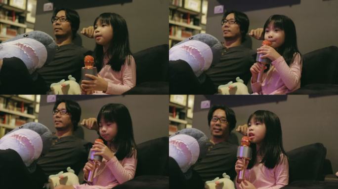 小女孩在她父亲的旁边唱歌，听客厅里的股票录像