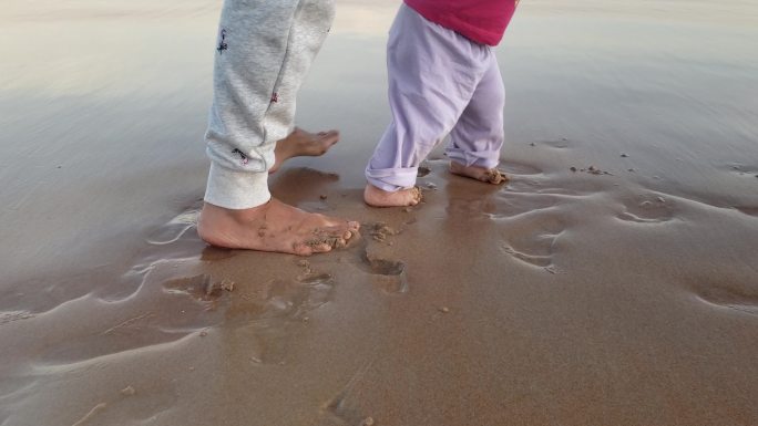 与母亲在海滩上赤脚走第一步的女婴双脚特写