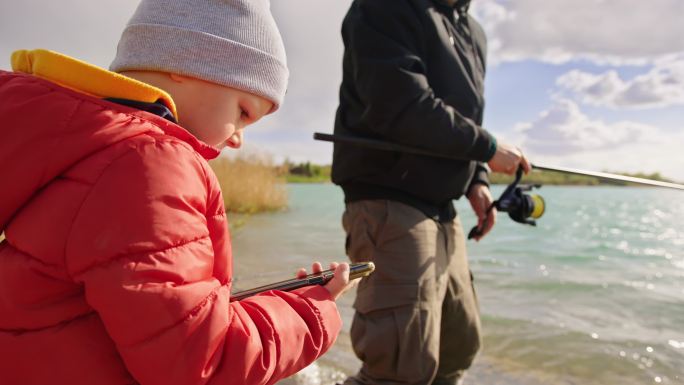 男子和儿子在河上用手机钓鱼