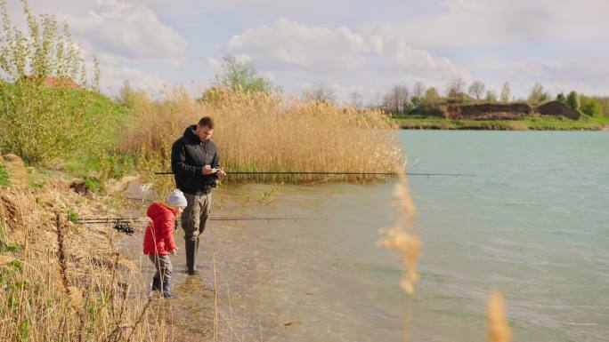 父子俩在河里钓鱼秋天国外父亲带孩子钓鱼玩
