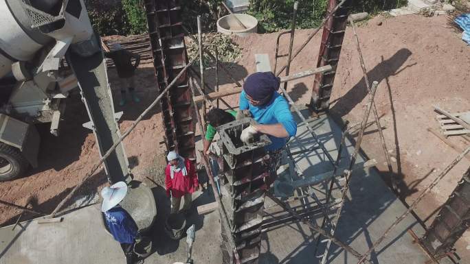 鸟瞰图。建筑工人在一个小型工地将混凝土泵入水泥柱模板。