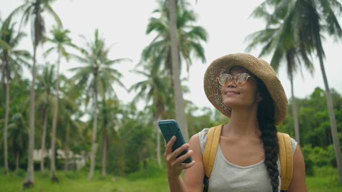 亚洲年轻女子探索椰子林，使用智能手机导航