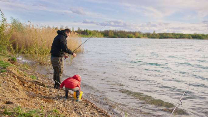 小男孩拿着鱼竿向河里扔鱼食