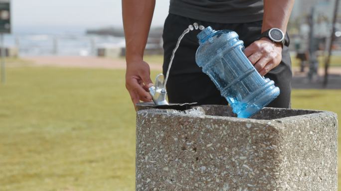 4k视频画面显示，一名男子外出跑步时在饮水机处给水瓶注水