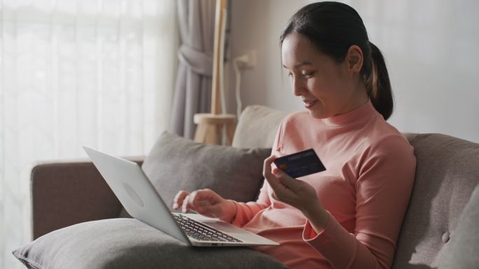 年轻的亚洲女性在家里用笔记本电脑上的信用卡在线购物