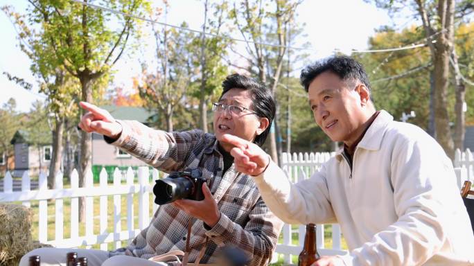 两个老年男人坐在房车露营院子里看数码相机