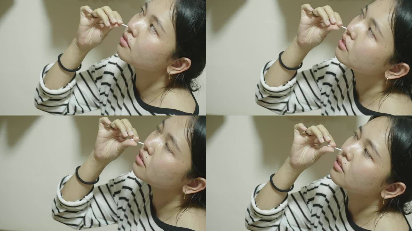 年轻的亚洲女性用棉签快速擦拭鼻子。