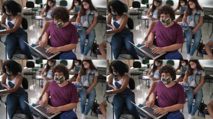 一个十几岁的男孩在教室里用笔记本电脑戴着口罩的照片
