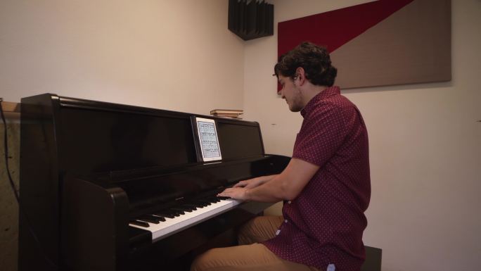 男音乐学生弹钢琴并从数字平板电脑上阅读