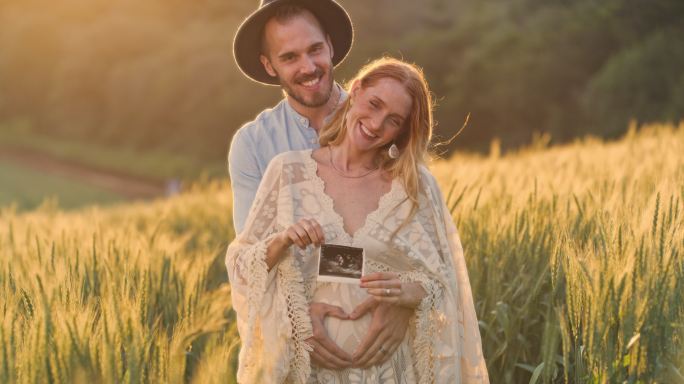 一位怀孕的年轻妇女和她的丈夫在农村的田野里做超声波检查。在大自然享受轻松产假的幸福夫妇