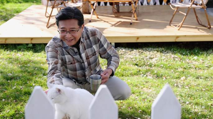 一个老年男人蹲在院子里和猫玩耍