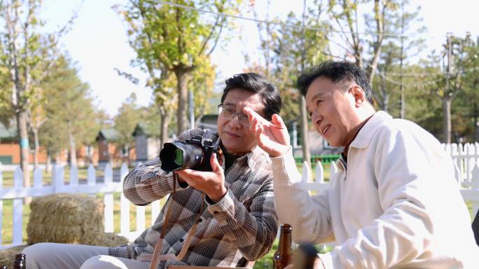 两个老年男人坐在房车露营院子里看数码相机