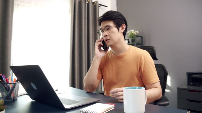 4k分辨率漂亮的亚洲成年男子在家办公时使用笔记本电脑在智能手机上与伴侣聊天时的慢动作，而在家中工作时