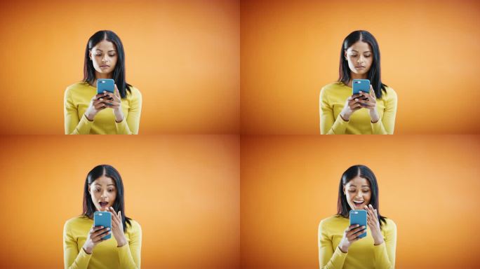 4k视频画面显示，一名年轻女子使用智能手机，在橙色的摄影棚背景下看起来很震惊