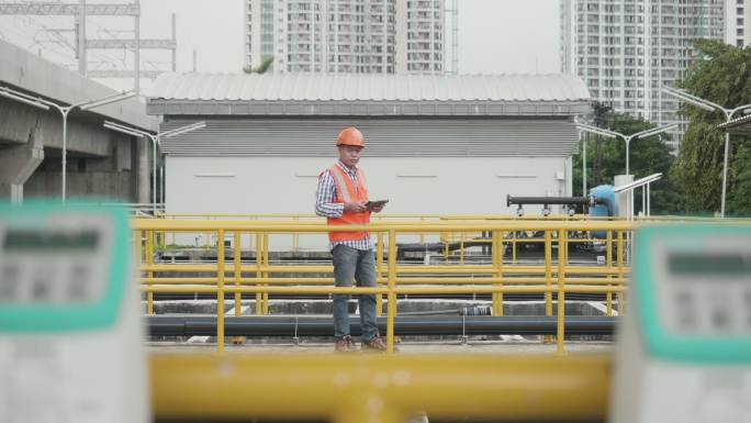 身穿反光背心和头盔的亚洲男工程师正在检查一家工业工厂的废水处理池。