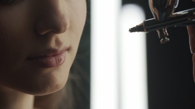 化妆师用喷枪在女孩脸上涂抹粉底。