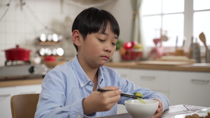 不开心的亚洲日本小男孩在看碗里的绿色蔬菜时做出厌恶的表情，摇头表示不喜欢，并将其放回餐桌