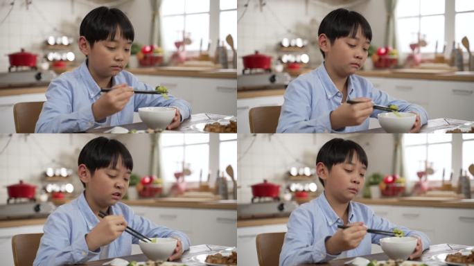 不开心的亚洲日本小男孩在看碗里的绿色蔬菜时做出厌恶的表情，摇头表示不喜欢，并将其放回餐桌