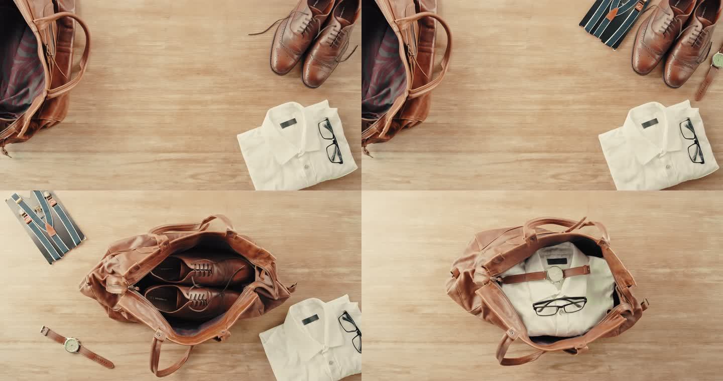 特写上方是一个打开的皮包，一件衬衫、鞋子、手表、吊带和眼镜被放在木地板上。把度假的衣服装在棕色皮包里
