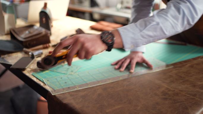 在裁缝车间工作时，无法辨认的男裁缝正在切割皮革
