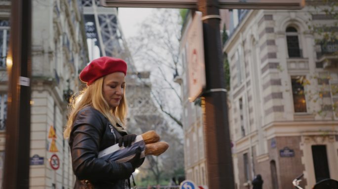 SLO MO穿着皮夹克的法国女人在埃菲尔铁塔上搬运法棍