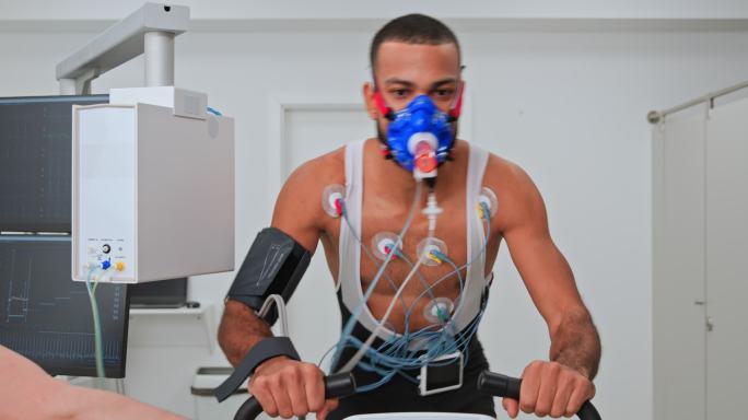 年轻的男运动员在诊所骑自行车测功仪，同时进行心肺压力测试