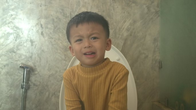 可爱的亚洲男婴坐在家里的马桶上