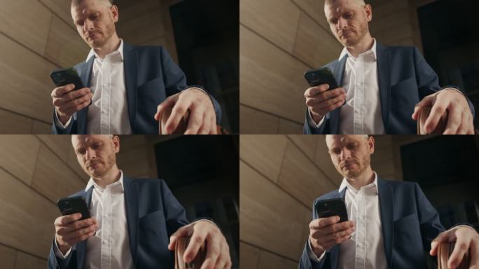 一位身穿蓝色西装的年轻商人在智能手机上打字的低角度视频